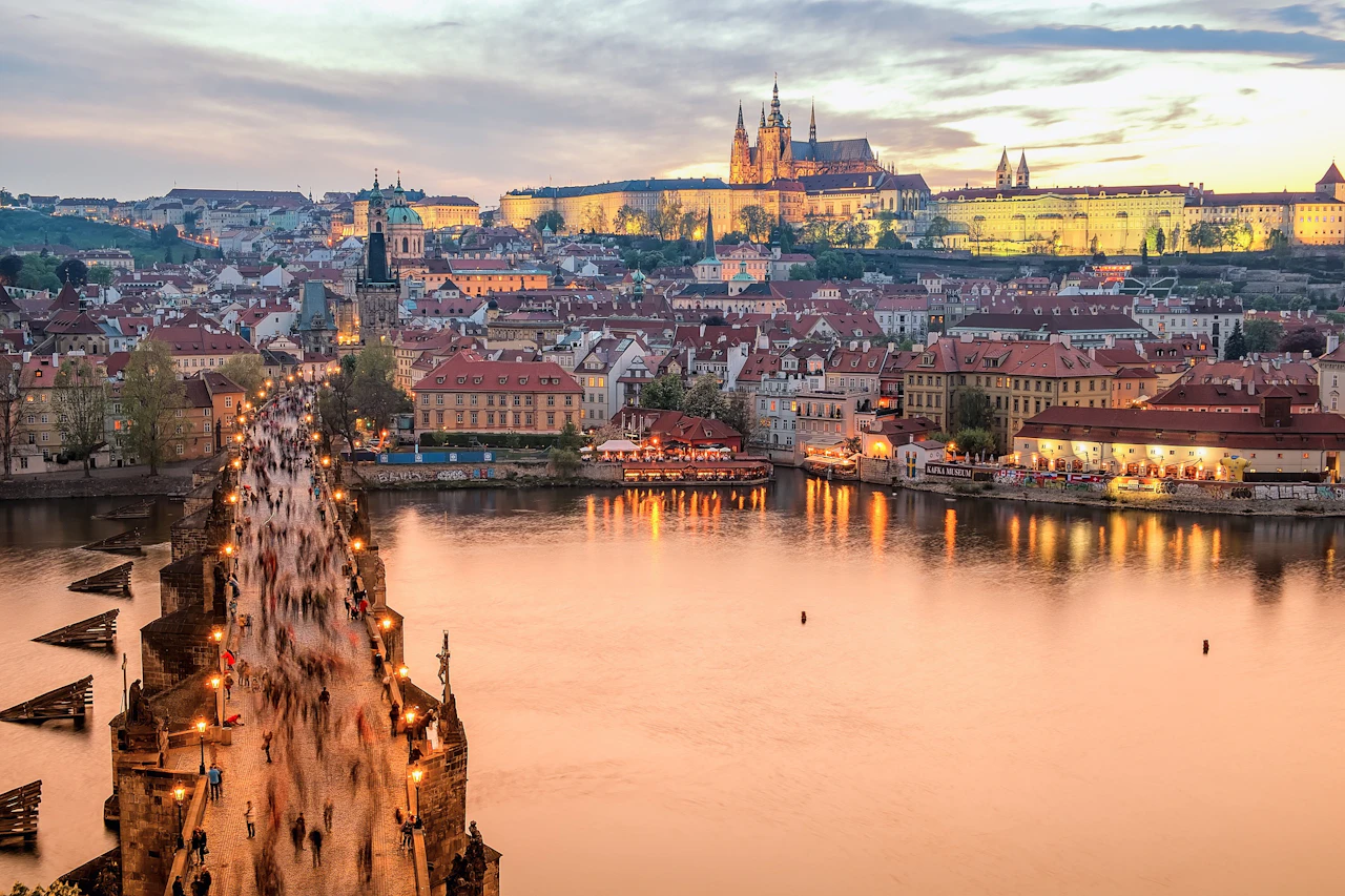 Charles Bridge crossing the Vltava toward Prague’s old rooftops and castle at sunset